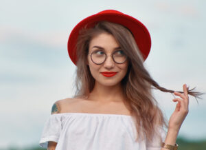אישה עם כובע אדום ומשקפיים מחייכת ומביטה הצידה