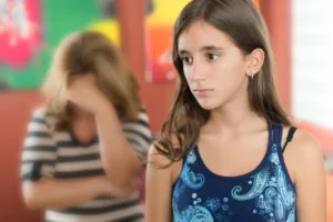 נערה במבט עצוב ומאחוריה אמא מרכינה ראש, מסתירה ומשדרת יאוש