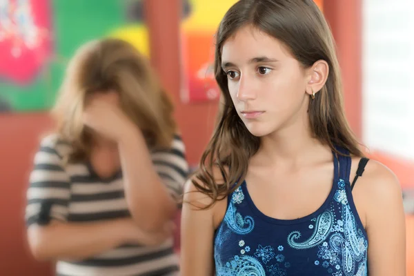 נערה במבט עצוב ומאחוריה אמא מרכינה ראש, מסתירה ומשדרת יאוש